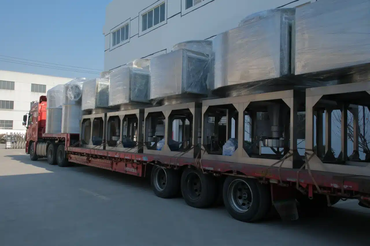 A red flatbed truck loaded with multiple XSG-14 spin flash dryers securely wrapped in protective film, parked outside an industrial building under clear skies.