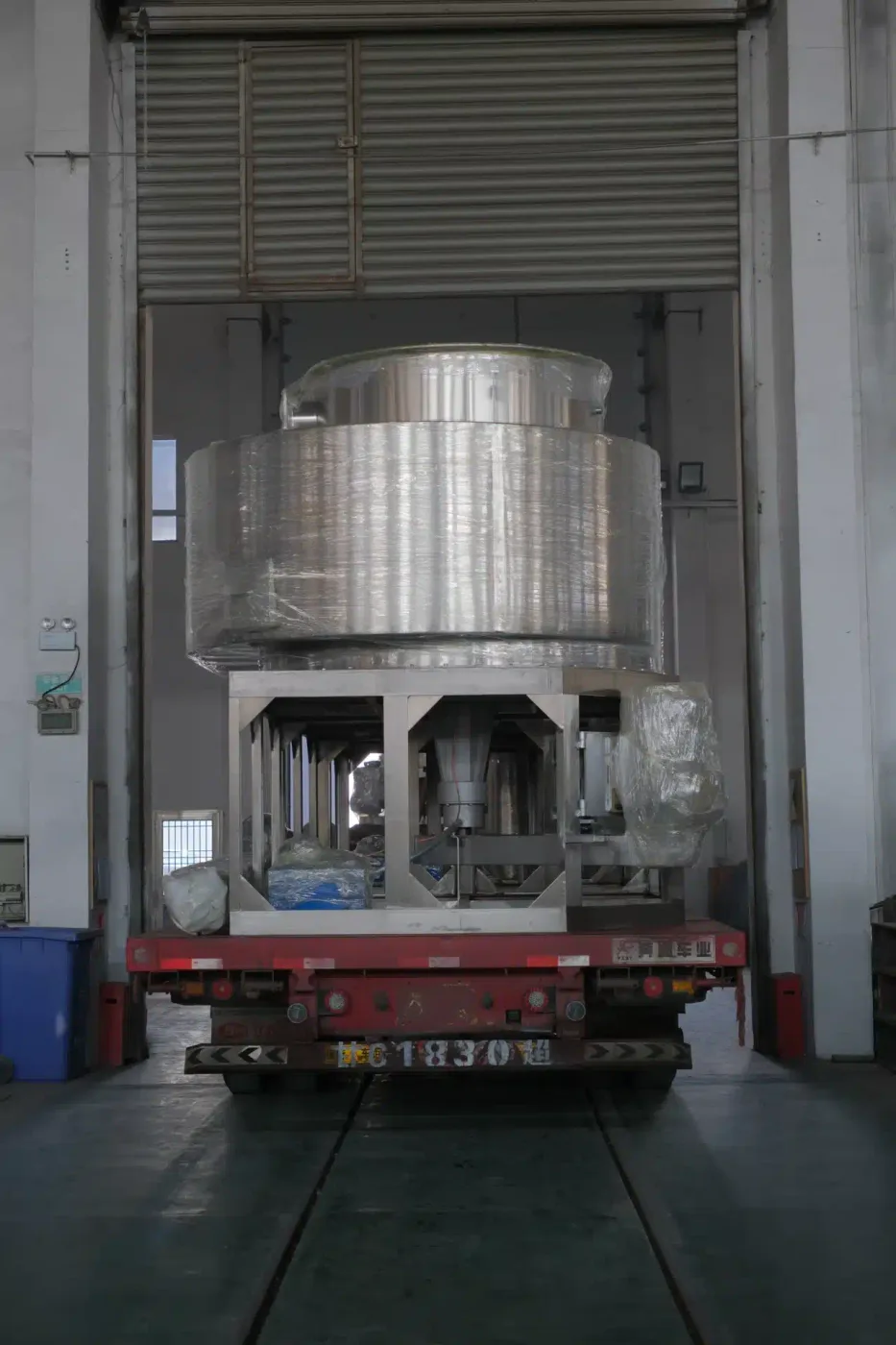 A spin flash dryer securely wrapped in protective material, loaded on a red flatbed truck inside an industrial facility, ready for delivery. 