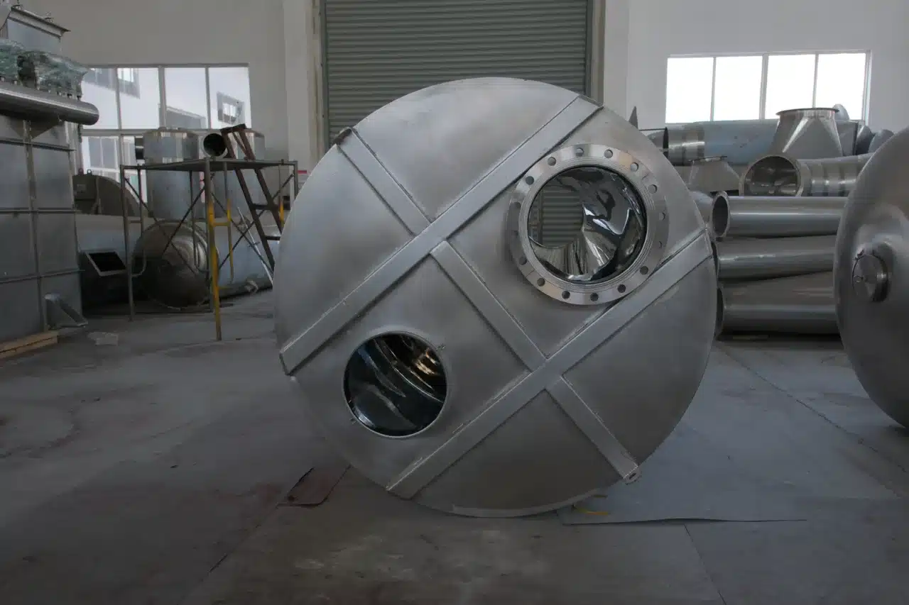  A stainless steel component of a spin flash dryer lying horizontally on the floor of an industrial workshop, showcasing its polished surface and circular openings.